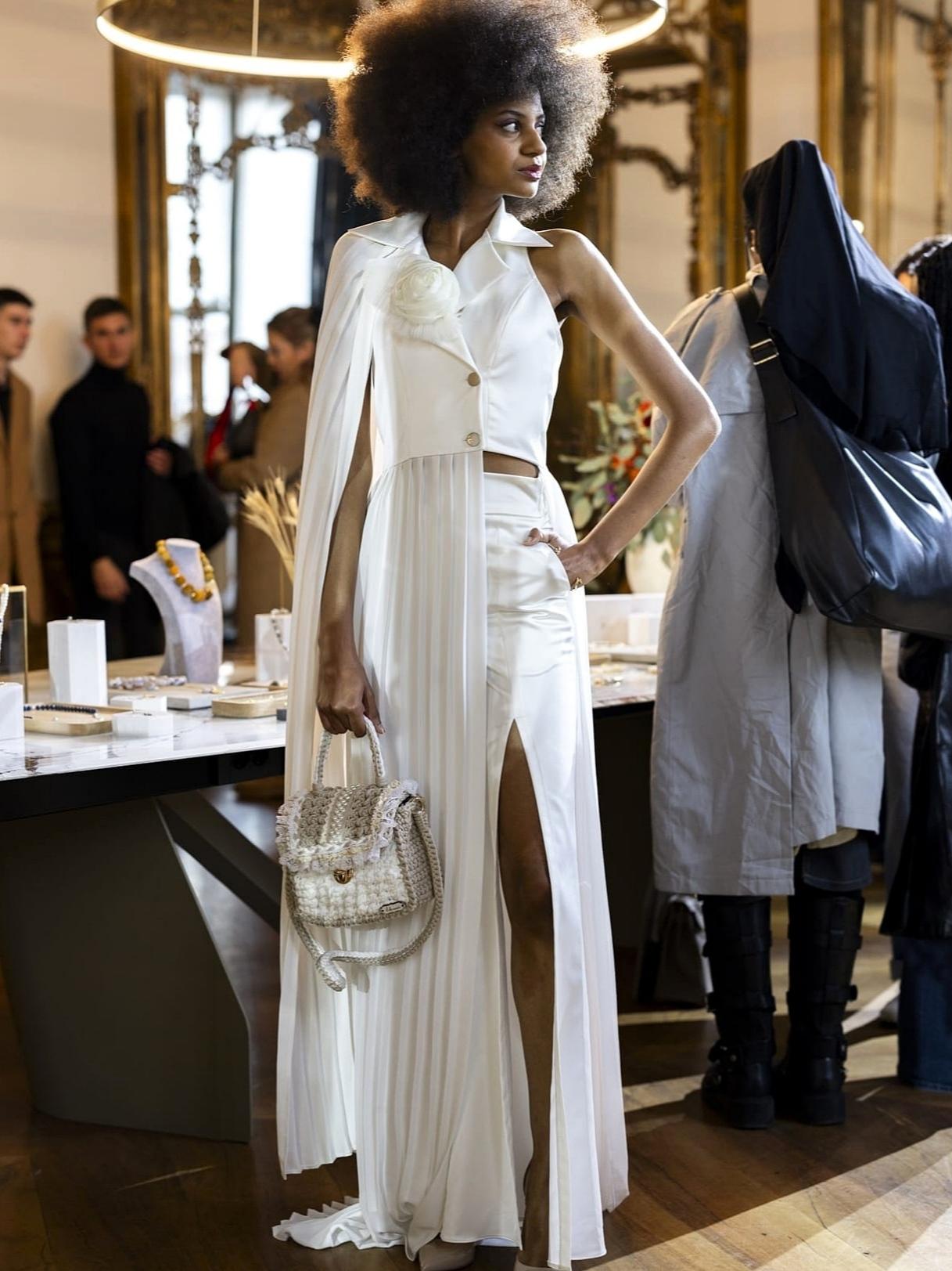 Model u bijeloj odjevnoj kombinaciji nosi svijetlu Bella Mandorla torbu na showroom izložbi tijekom Milan Fashion Weeka